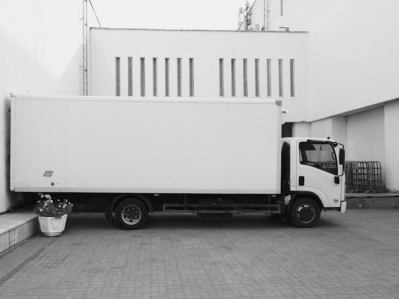 Weißer Koffer-LKW vor einem Gebäude (vorher, Symbolbild)
